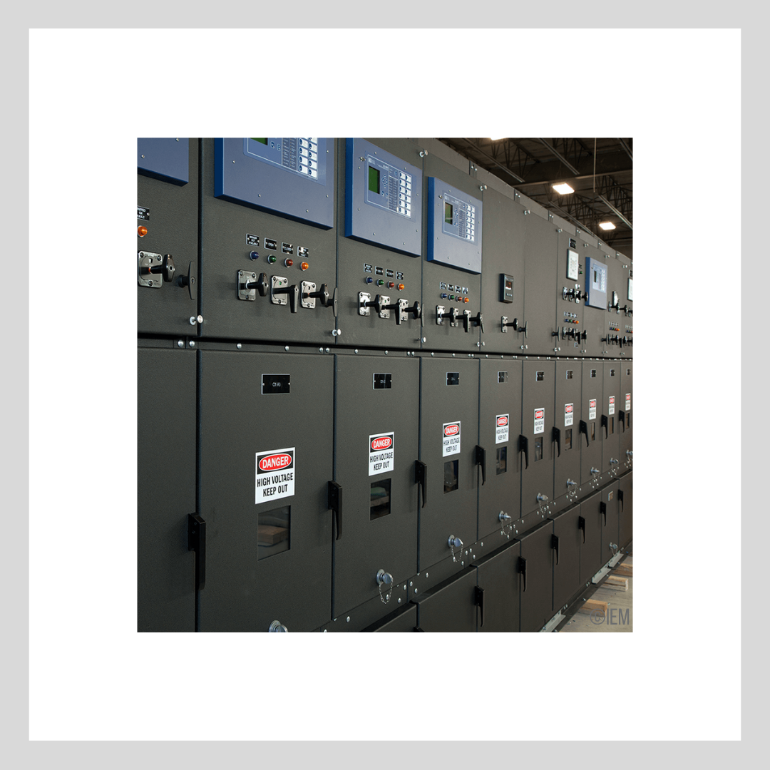 Exterior of wall filled with large, black high voltage substations with access panels, computer interfaces, and 'danger' signs on the front.