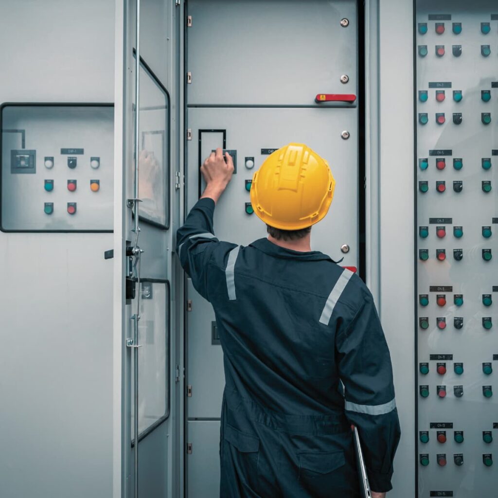 Person wearing a yellow hard hat facing an electrical panel adjusting a setting