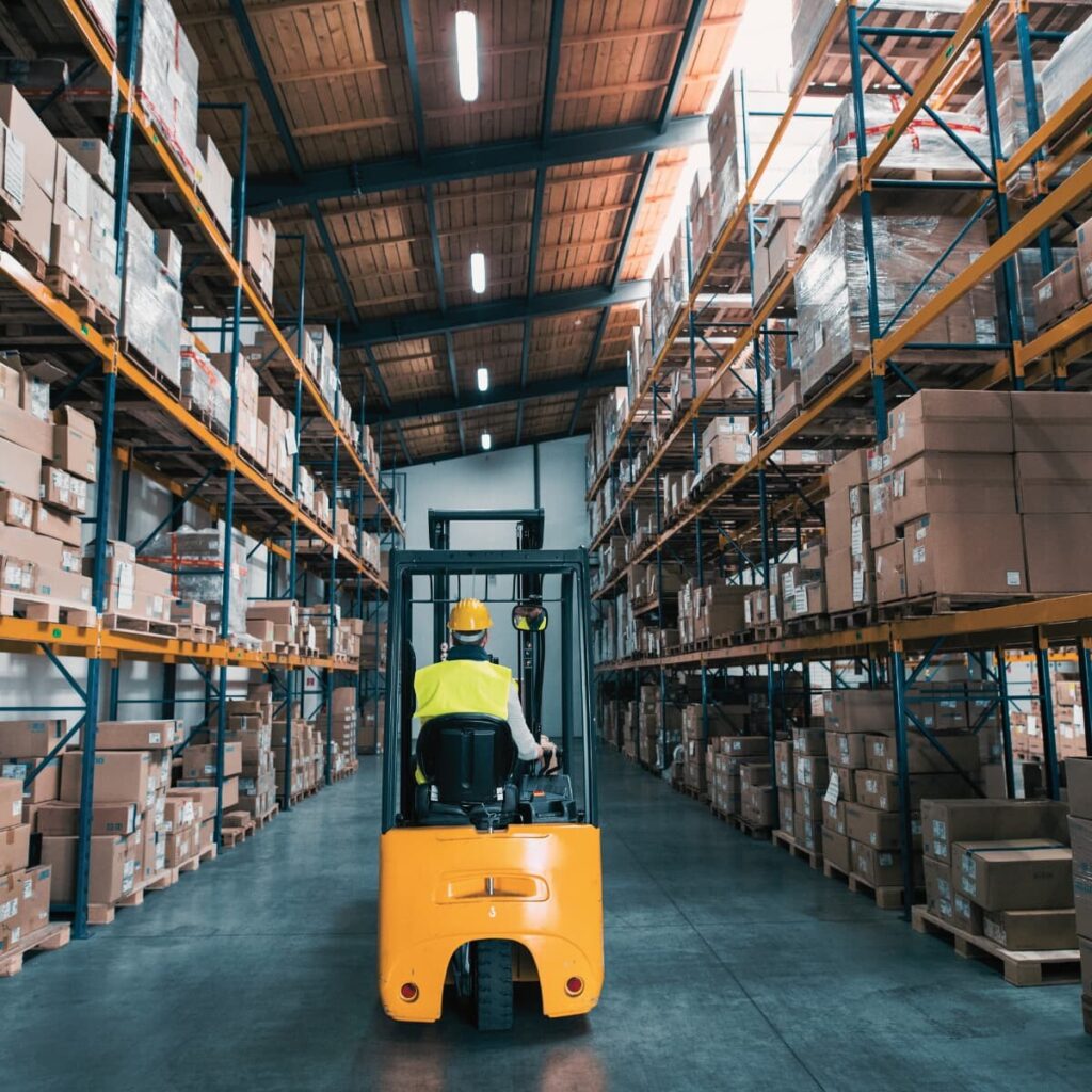 Interior of a warehouse with stock on shelves and a forklift driving down the center of the row