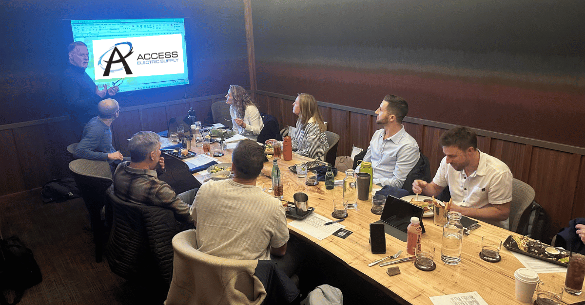 Sales team surrounding a table while one person presents a slide show